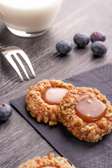 Peanut shortbread cookies with caramel jam inside on a black napkin with blueberries and dessert fork and milk