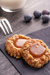 Peanut shortbread cookies with caramel jam inside on a black napkin with blueberries and dessert fork and milk