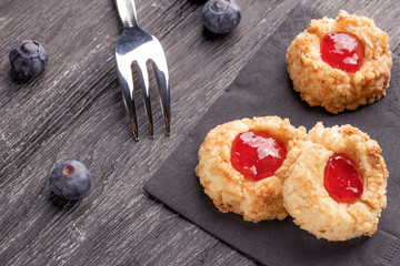 Cookies made from hazelnut shortcake with strawberry jam inside on a black napkin with blueberries