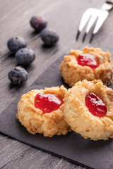 Cookies made from hazelnut shortcake with strawberry jam inside on a black napkin with blueberries