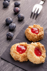 Cookies made from hazelnut shortcake with strawberry jam inside on a black napkin with blueberries