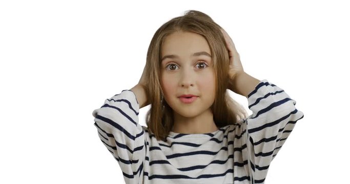 Close up of the cute teen girl with long hair in the striped blouse holding her head with hands and doing surprised or scarry face on the white wall background.