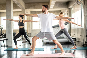 Teamwork of young women and young man doing yoga exercises in gym concept healthy life fitness for slim