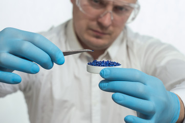A man in a white coat holding tweezers and plastic pellets and granules in the laboratory.