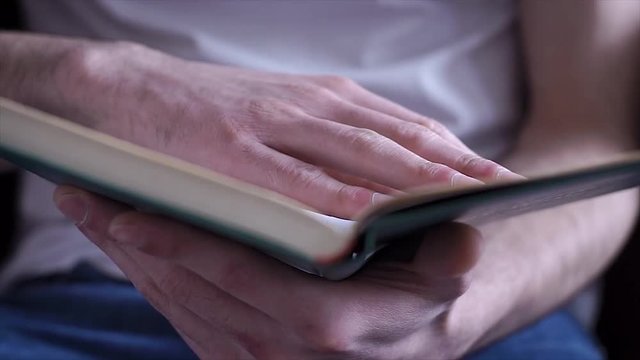 Hand and book: reading a book and holding your fingers along the lines. A man's hand holds a book and moves his fingers along the page while reading. The reader of the book holds