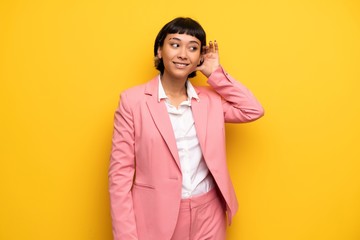 Modern woman with pink business suit listening to something by putting hand on the ear