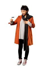 A full-length shot of a Short hair woman with coat holding a credit card and surprised over isolated white background
