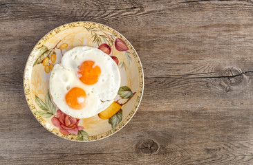 Two fried eggs in the colorful plate on the old wooden background.