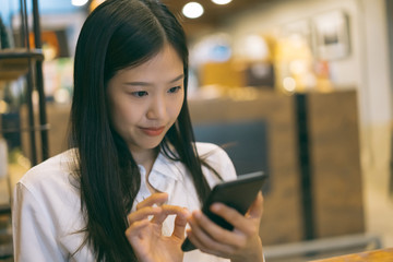 Young Asian woman using phone at a coffee shop happy and smile.