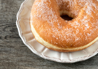 Sweet fried donut covered with sugar on plate on the old wooden background.