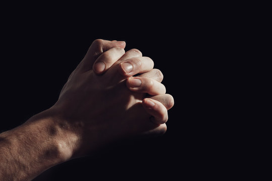 Hand of praying man isolated on black background.
