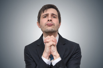 Funny young businessman is begging or asking for help.