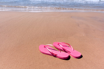 pink flip-flops on yellow sand at the water's edge on the beach