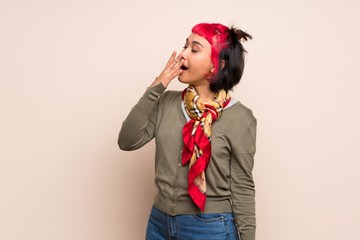 Young woman with pink hair over yellow wall yawning and covering wide open mouth with hand