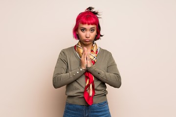 Young woman with pink hair over yellow wall keeps palm together. Person asks for something