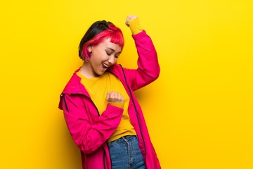 Young woman with pink hair over yellow wall celebrating a victory