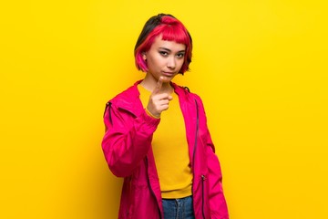 Young woman with pink hair over yellow wall frustrated and pointing to the front