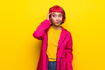 Young woman with pink hair over yellow wall with an expression of frustration and not understanding