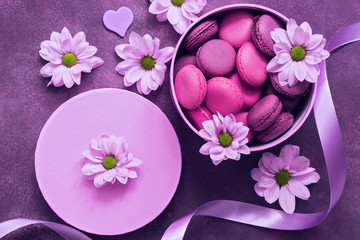 Fototapeta na wymiar Purple and pink macaroons in a gift box on a beautiful purple background decorated with flowers. Top view