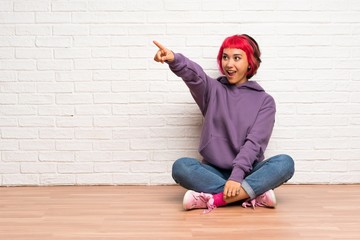 Young woman with pink hair sitting on the floor pointing away