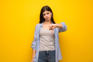 Teenager girl over yellow wall showing thumb down with negative expression