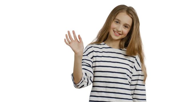 Close up of the blonde teenager girl with long hair in the striped blouse waving her hand and smiling on the white wall background. Portrait.