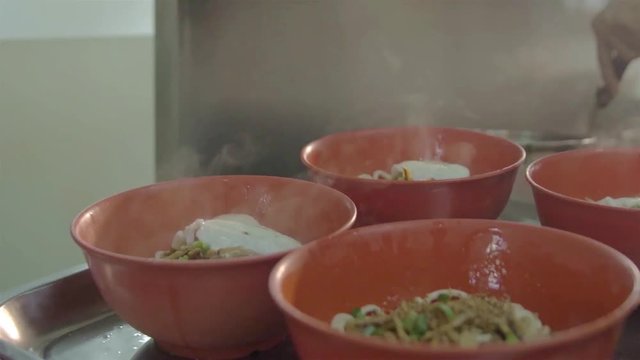 Asian Guy Putting Hot Eggs On Top Of A Red Beef Noodle Bowl - Side View  