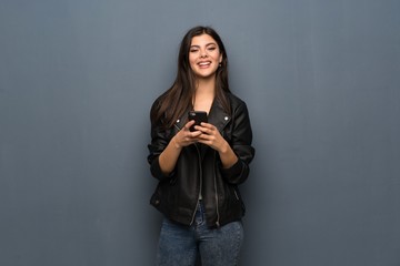 Teenager girl over grey wall sending a message with the mobile