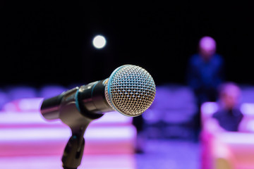 Wireless microphone on the stand. Blurred background. People in the audience. Show on stage in the theater or concert hall.