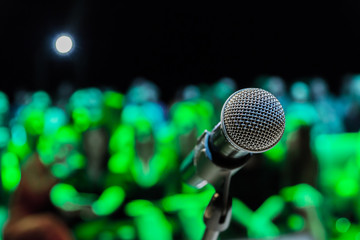 Wireless microphone on the stand. Blurred background. People in the audience. Show on stage in the theater or concert hall.