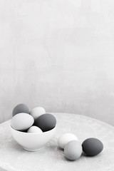 Gray eggs lie in a white bowl on a gray background. Gradient color from white to black. Minimal...