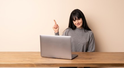 Young woman working with her laptop showing and lifting a finger in sign of the best