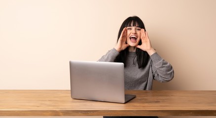Young woman working with her laptop shouting and announcing something