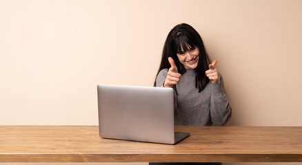 Young woman working with her laptop pointing to the front and smiling