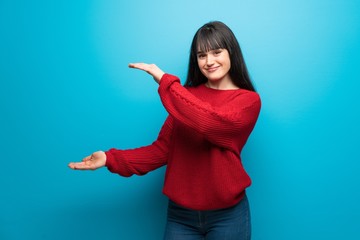 Woman with red sweater over blue wall holding copyspace to insert an ad