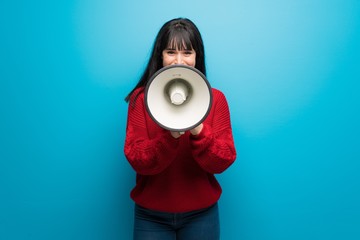 Woman with red sweater over blue wall shouting through a megaphone