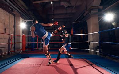 Two sportsmen kickboxers exercising kickboxing in the ring at the sport club