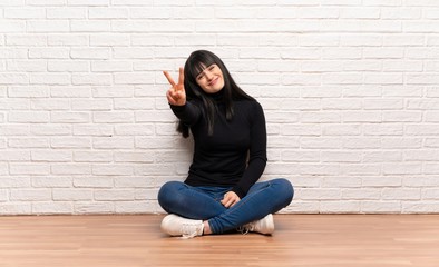 Woman sitting on the floor smiling and showing victory sign