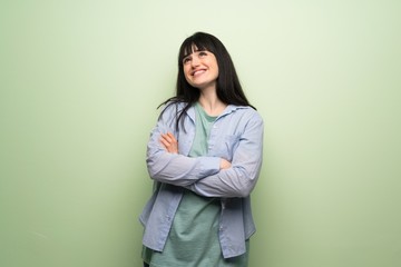 Young woman over green wall looking up while smiling