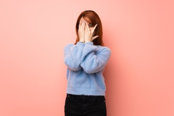 Young redhead woman over pink background covering eyes by hands and looking through the fingers