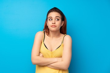 Fototapeta na wymiar Young redhead woman over blue background making doubts gesture while lifting the shoulders