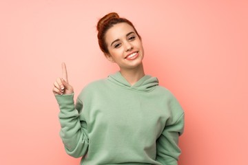 Young redhead woman with sweatshirt showing and lifting a finger in sign of the best
