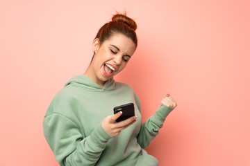 Young redhead woman with sweatshirt with phone in victory position