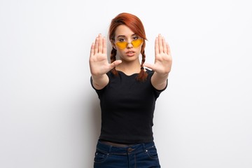 Young redhead woman over white wall making stop gesture and disappointed