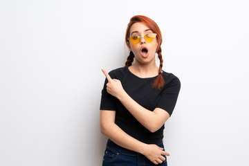 Young redhead woman over white wall surprised and pointing side