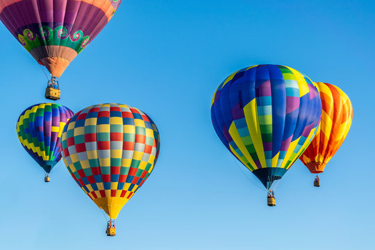 An image of a number of bright colored hot air balloons taking flight in the early morning sun.
