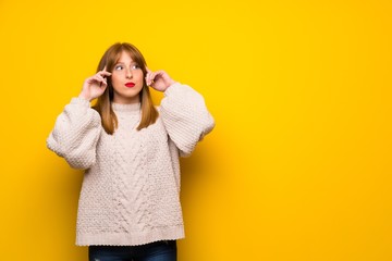 Redhead woman over yellow wall having doubts and thinking