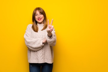 Redhead woman over yellow wall smiling and showing victory sign