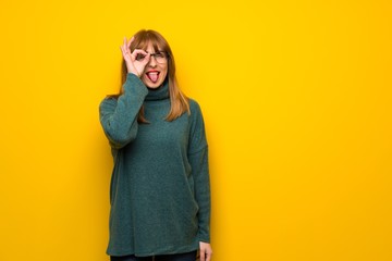 Woman with glasses over yellow wall makes funny and crazy face emotion