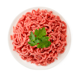 Minced meat in a plate and parsley leaves on a white. The form of the top.